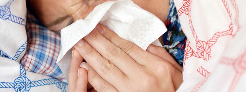 Eine Frau liegt im Bett und putzt sich die Nase. Akute Atemwegserkrankungen kursieren zur Zeit. - Foto: Maurizio Gambarini/dpa