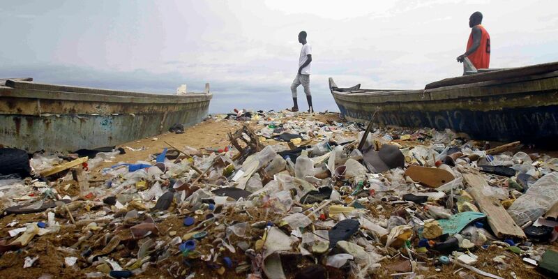 Menschen spazieren über einen mit Plastik verschmutzten Strand an der Elfenbeinküste. - Foto: Diomande Ble Blonde/AP/dpa