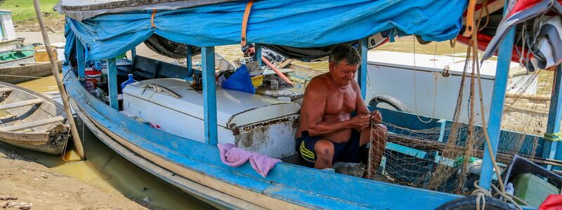 Ein Fischer sitzt fast im Trockenen in seinem Boot und flickt ein Netz. Die Dürre bereitet den Flussbewohnern nicht nur Schwierigkeiten beim Fischen, sondern auch beim Verkehr. Dörfer sind in der Region über die Flüsse vernetzt. - Foto: Aguilar Abecassis/dpa