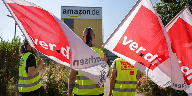 Streikende stehen mit Verdi-Flaggen vor einem Verteilzentrum des Online-Händlers Amazon in Leipzig (Archivbild). - Foto: Jan Woitas/dpa