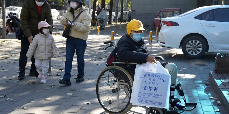 Ein Junge in einem Rollstuhl hält in Peking eine Tasche aus der radiologischen Abteilung eines Kinderkrankenhauses. In den vergangenen Tagen hatten Berichte über die starke Häufung von Atemwegserkrankungen bei Kindern Sorgen aufkommen lassen. - Foto: Ng Han Guan/AP/dpa