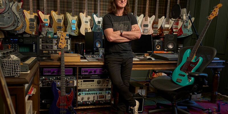 Der Rush-Frontmann Geddy Lee steht in seinem Studio, Bassgitarren hängen an der Wand. - Foto: HarperCollins