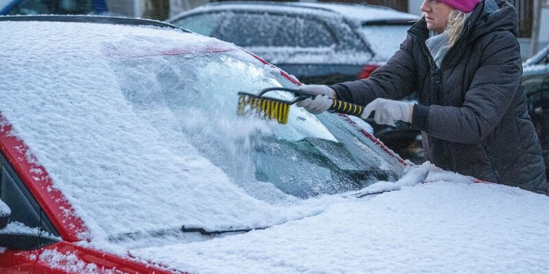Eine Frau in München befreit am frühen Morgen ein Auto von Schnee und Eis. Auch in den kommenden Tagen soll es winterlich bleiben. - Foto: Stefan Puchner/dpa