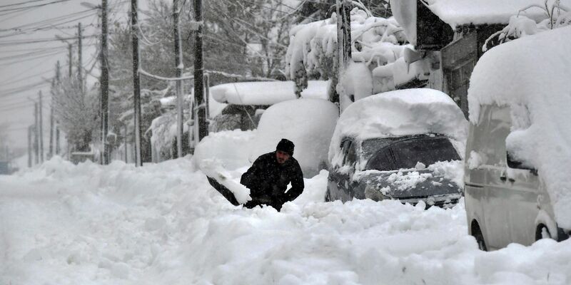 Ein Mann in Isperich schaufelt Schnee, um sein Auto zu befreien. - Foto: Mehmed Aziz/AP/dpa