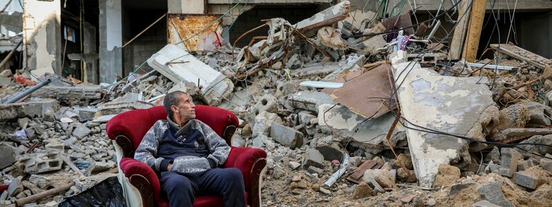 Ein palästinensischer Mann sitzt in einem Sessel vor einem zerstörten Gebäude in Gaza-Stadt. - Foto: Mohammed Hajjar/AP/dpa