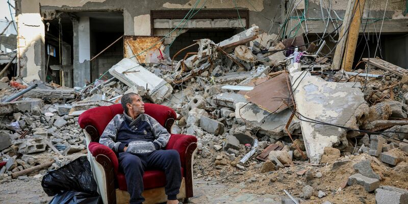 Ein palästinensischer Mann sitzt in einem Sessel vor einem zerstörten Gebäude in Gaza-Stadt. - Foto: Mohammed Hajjar/AP/dpa