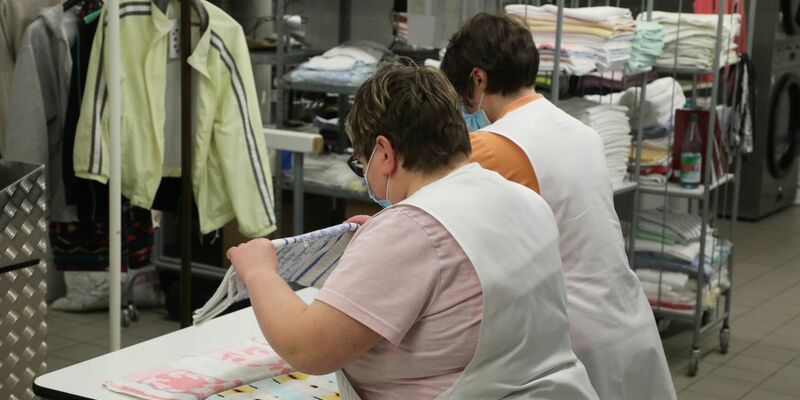 Zwei Frauen arbeiten in der Wäscherei der Lebenshilfe Gera e.V und legen dort Wäsche zusammen. - Foto: Bodo Schackow/dpa-Zentralbild/dpa
