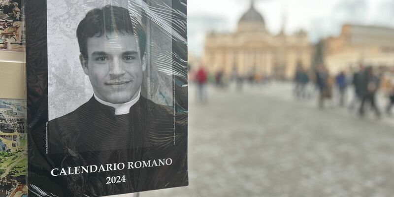 Der «Calendario Romano» an einem Souvenirstand, im Hintergrund der Petersdom. - Foto: Christoph Sator/dpa