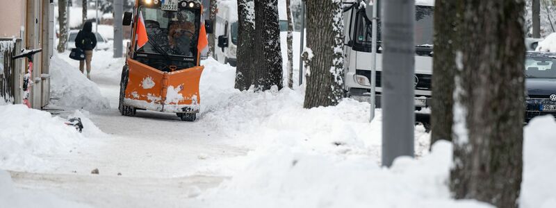 Ein Räumfahrzeug fährt über einen verschneiten Weg in München. - Foto: Lukas Barth/dpa