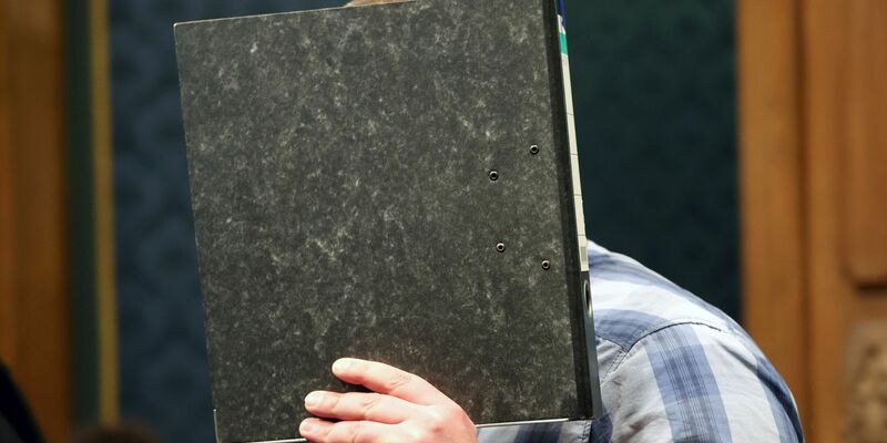 Der angeklagte Feuerwehrmann mit einem Aktendeckel vor dem Gesicht im Gerichtssaal. - Foto: Bernd Wüstneck/dpa