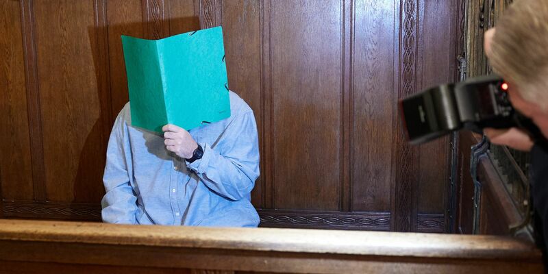 Der Angklagte sitzt im Landgericht Berlin und verbirgt sein Gesicht hinter einem Schnellhefter. - Foto: Joerg Carstensen/dpa