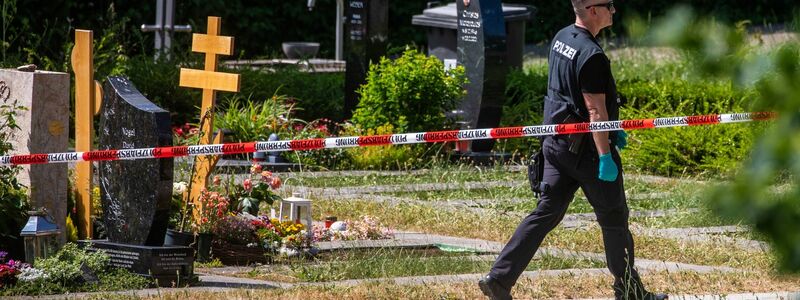 Ein Polizist geht über den abgesperrten Teil an einem Tatort auf einem Friedhof. - Foto: Christoph Schmidt/dpa