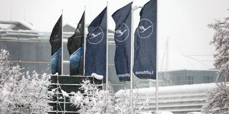 Fahnen der Lufthansa wehen am  Flughafen München im Schneetreiben. Die deutsche Fluggesellschaft kauft neue Maschinen ein. - Foto: Karl-Josef Hildenbrand/dpa
