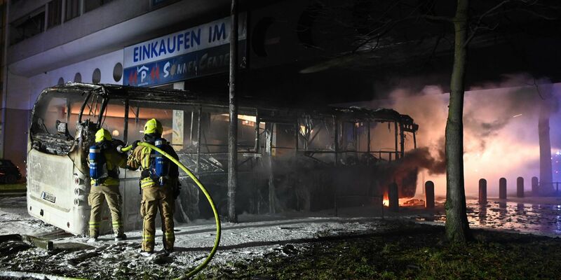 Einsatzkräfte der Feuerwehr löschen in der Silvesternacht 2022/2023 im Bezirk Berlin-Neukölln einen brennenden Bus, der von Unbekannten angezündet worden war. - Foto: Paul Zinken/dpa
