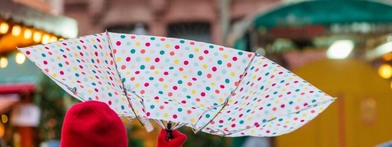 Vom Wind verweht: Eine Frau geht mit einem Regenschirm über einen Weihnachtsmarkt in Frankfurt. - Foto: Andreas Arnold/dpa