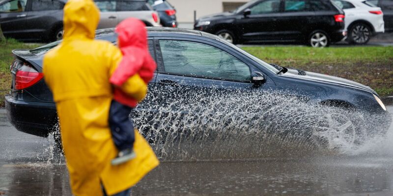 Eine Mutter und ihr Kind blicken auf eine teils überflutete Straße in Osnabrück. - Foto: Friso Gentsch/dpa