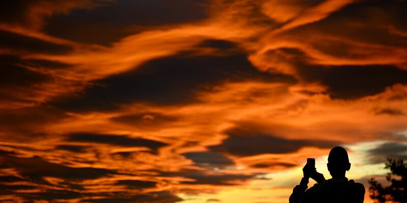 Das Naturschauspiel festhalten: Ein Mann fotografiert einen Sonnenuntergang. - Foto: Laurent Gillieron/KEYSTONE/dpa