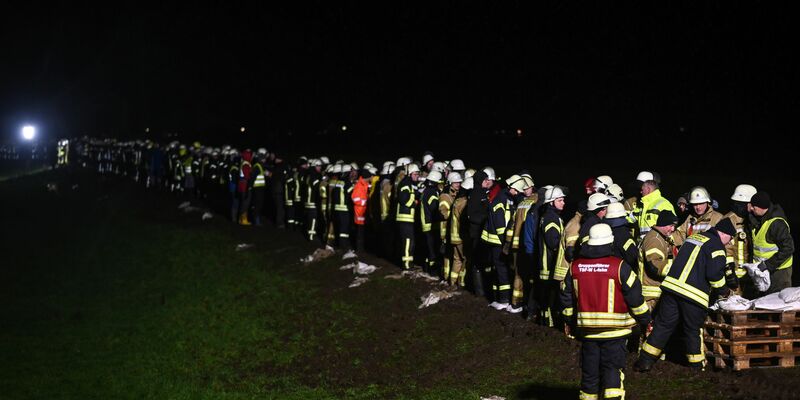 Mit einer Menschenkette werden gefüllte Sandsäcke zu den Bruchstellen gebracht. - Foto: Lars Penning/dpa
