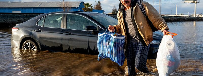 Ein Mann trägt im Januar in Merced, Kalifornien, Habseligkeiten aus seinem überfluteten Haus. - Foto: Noah Berger/AP/dpa