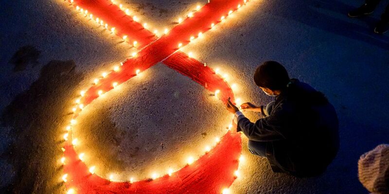 Eine Frau stellt Kerzen auf, die eine rote Schleife formen - ein weltweit anerkanntes Symbol für die Solidarität mit HIV-Infizierten. - Foto: Sunil Pradhan/SOPA Images via ZUMA Wire/dpa