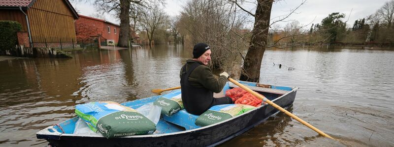 Ein Anwohner bringt mit einem kleinen Ruderboot Futter für seine Tiere über eine überschwemmte Straße in Hagen-Grinden zu seinem Hof. - Foto: Christian Charisius/dpa