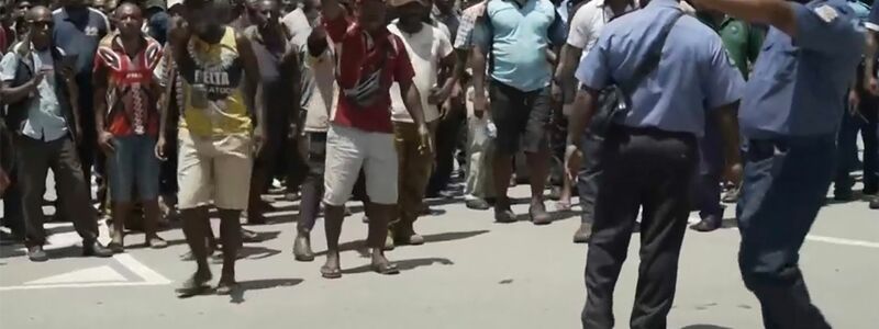 Das Videostandbild zeigt zwei Polizisten neben einer aufgebrachten Menschenmenge in Port Moresby. - Foto: Uncredited/Australian Broadcasting Corp/AP/dpa