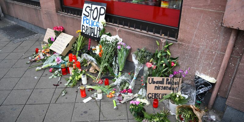 Blumen, Kerzen und Schilder liegen in Mannheim an dem Ort, an dem ein Mann Anfang Mai 2022 nach einer Polizeikontrolle starb. - Foto: René Priebe/PR-Video /dpa