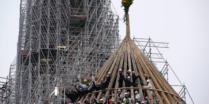 Arbeiter feiern den Abschluss des Wiederaufbaus des Dachstuhls der Kathedrale Notre Dame mit einem traditionellen Blumenstrauß. - Foto: Christophe Ena/AP/dpa