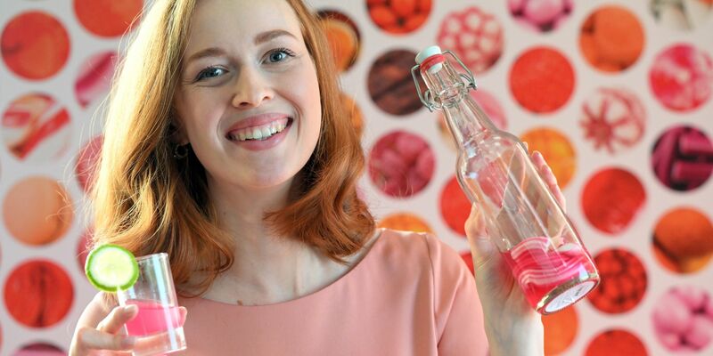 Model Christin hält auf der  Internationalen Süßwarenmesse ein Glas Wodka in der Hand, das mit Sweet Shots-Bonbonmasse versetzt wurde. - Foto: Federico Gambarini/dpa
