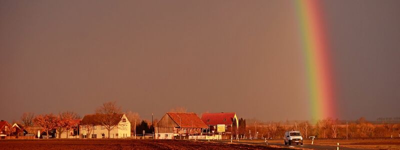 Ein Sturmtief kündigt sich bei tief stehender Sonne mit starkem Wind an, während sich ein Regenbogen am Himmel gebildet hat. - Foto: Matthias Bein/dpa