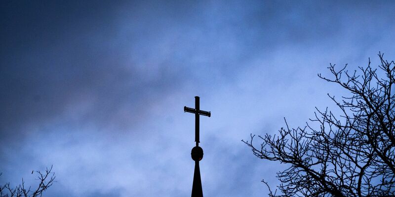 Dunkle Wolken über einem Kreuz einer Kirche: Einem der Missbrauchsopfer muss Schadenersatz gezahlt werden (Symbolbild). - Foto: Julian Stratenschulte/dpa