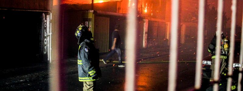 Ein Feuerwehrmann blickt nach oben, als die Flammen eines Waldbrandes auf Gebäude übergreifen. - Foto: Cristobal Basaure/AP