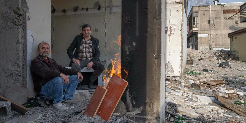 Zwei Männer wärmen sich in den Trümmern eines zerstörten Hauses in Kahramanmaras an einem Feuer. Im Zentrum der Stadt waren bei dem Beben vor einem Jahr unzählige Häuser zerstört oder beschädigt worden. - Foto: Boris Roessler/dpa
