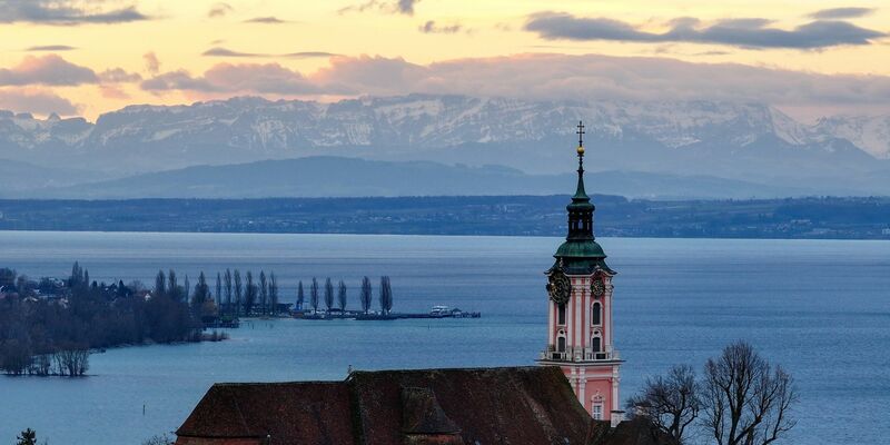 Hinter der ehemaligen Klosterkirche Birnau am Bodensee geht die Sonne auf. Die Alpen sind im Hintergrund zu sehen. - Foto: Felix Kästle/dpa