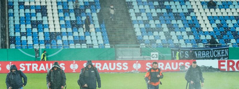 Im Ludwigspark-Stadion versuchen Helfer, Wasserlachen vom Spielfeld zu entfernen. - Foto: Uwe Anspach/dpa