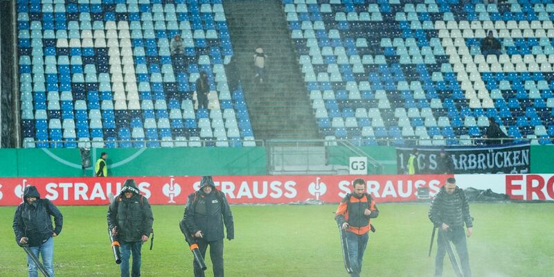 Im Ludwigspark-Stadion versuchen Helfer, Wasserlachen vom Spielfeld zu entfernen. - Foto: Uwe Anspach/dpa