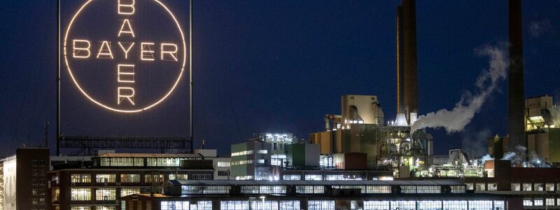 Das Bayer-Kreuz, das Logo des Unternehmens, leuchtet auf dem Werksgelände von Bayer in Leverkusen. - Foto: Thomas Banneyer/dpa