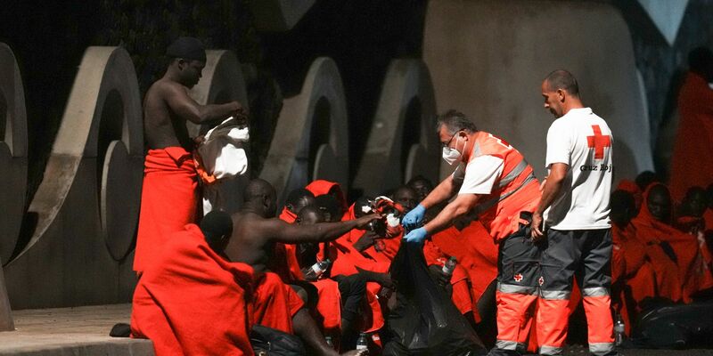 Mitarbeiter des Roten Kreuzes verteilen im November Wasser an Migranten an einer Anlegestelle im Hafen von La Restinga auf der kanarischen Insel El Hierro. - Foto: Humberto Bilbao/AP/dpa