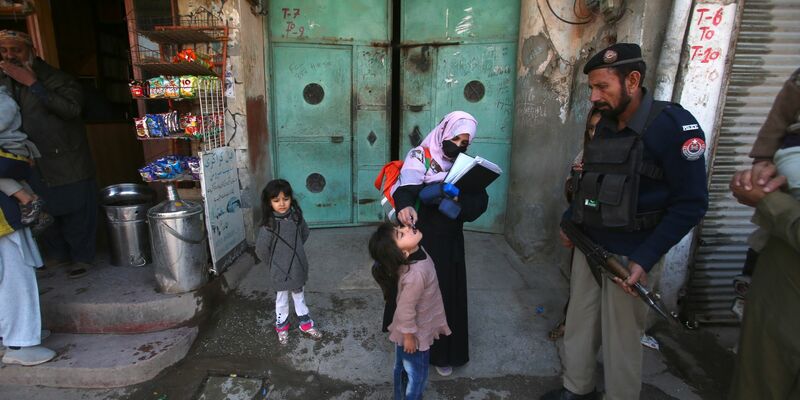 Ein Polizist in Pakistan steht Wache, während einem Kind ein Polio-Impfstoff verabreicht wird. - Foto: Muhammad Sajjad/AP/dpa