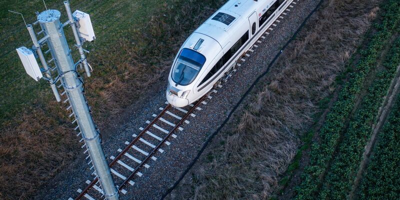 Ein Testzug der Deutschen Bahn fährt an einer der Antennenmasten für das 5G-Bahnprojekt vorbei. - Foto: Jens Büttner/dpa