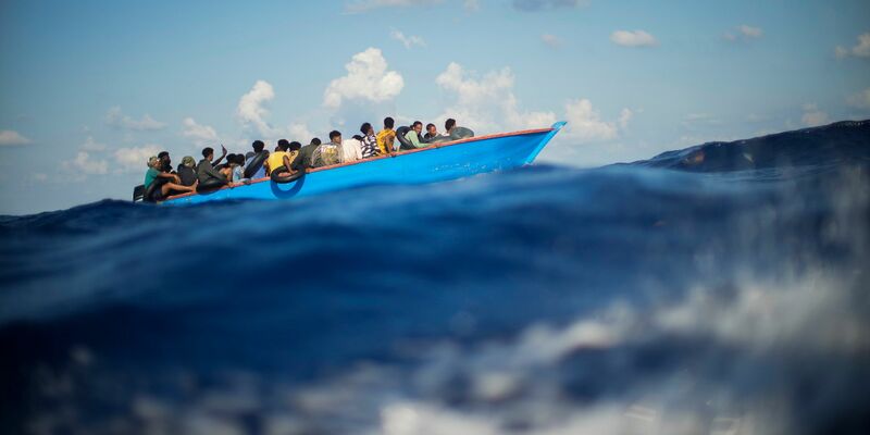 Migranten sitzen in einem Holzboot im Mittelmeer nahe der Insel Lampedusa: Die kleine Insel gehört seit Jahren zu den Brennpunkten illegaler Migration (Archivfoto). - Foto: Francisco Seco/AP/dpa