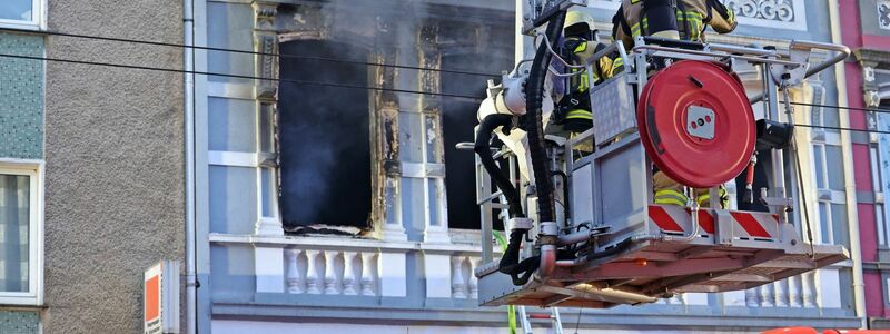 Feuerwehrmänner stehen vor dem Mehrfamilienhaus, in dem es gebrannt hat. - Foto: Gianni Gattus/Blaulicht Solingen/dpa