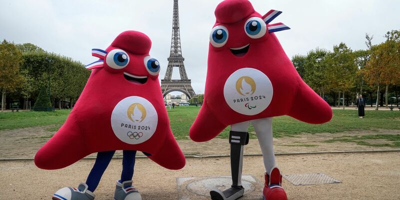 Die Maskottchen der Olympischen (l) und Paralympischen Spiele in Paris stehen vor dem Eiffelturm. - Foto: Michel Euler/AP/dpa