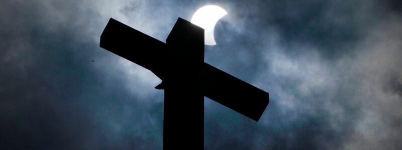 Wolken lösen sich auf und geben über dem Kreuz eines Kirchturms in Manor (Texas) den Blick auf die beginnende Sonnenfinsternis frei. - Foto: Charles Rex Arbogast/AP