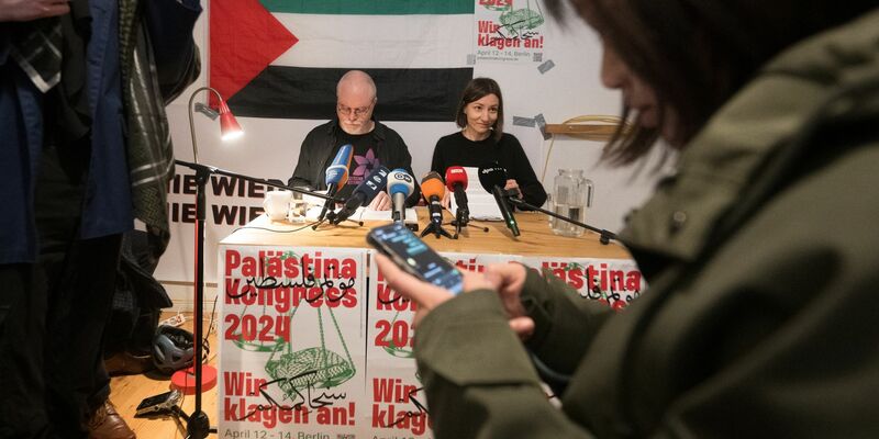 Teilnehmer sitzen vor Beginn des Palästina-Kongress 2024 im Veranstaltungsraum vor einem Plakat des Kongresses. - Foto: Sebastian Christoph Gollnow/dpa