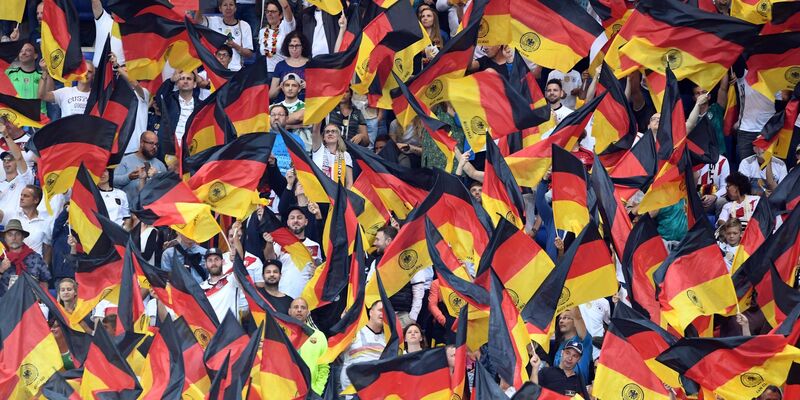 Fans schwenken Deutschlandfahnen auf der Tribüne. - Foto: Uli Deck/dpa
