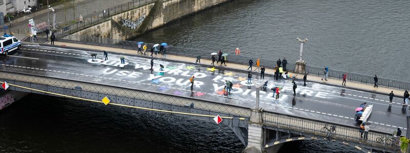 Klimaaktivisten der Bewegung Fridays for Future malen auf der Marschallbrücke in Berlin den Schriftzug «Our world is on fire - use your voice!». - Foto: Christophe Gateau/dpa