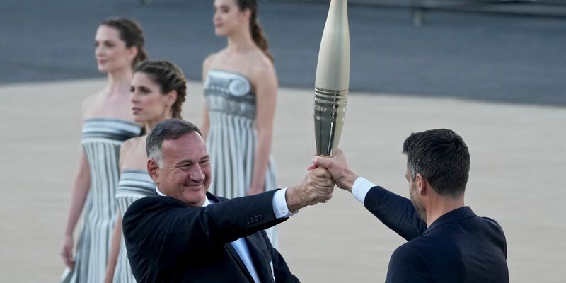 Der Präsident des französischen Organisationskomitees, Tony Estanguet (r), nahm die olympische Flamme in Athen entgegen. - Foto: Petros Giannakouris/AP/dpa