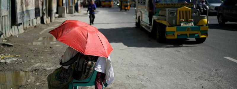 Eine Straßenverkäuferin schützt sich in Manila mit einem Regenschirm vor der Sonne. - Foto: Aaron Favila/AP/dpa
