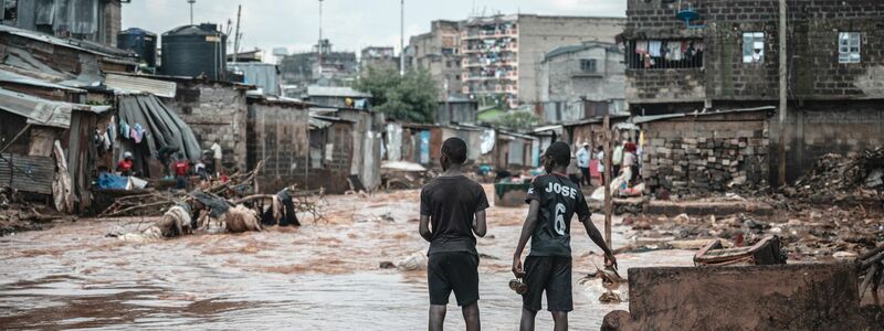 Menschen stehen am Ufer eines überfluteten Flusses in den Mathare-Slums in Nairobi. - Foto: Wang Guansen/XinHua/dpa